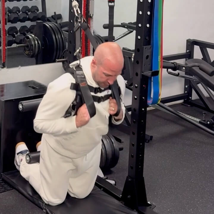 Person in a white tracksuit using a weight machine in a gym.